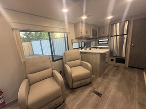 Eine kompakte Küchenzeile für Wohnmobile mit einer zentralen Kücheninsel, zwei beigefarbenen Sesseln und einem Edelstahlkühlschrank.