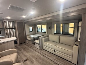 Ein kompaktes Wohnmobil-Interieur mit Küchenzeile, Essbereich, Sitzgruppe und einem Fenster.