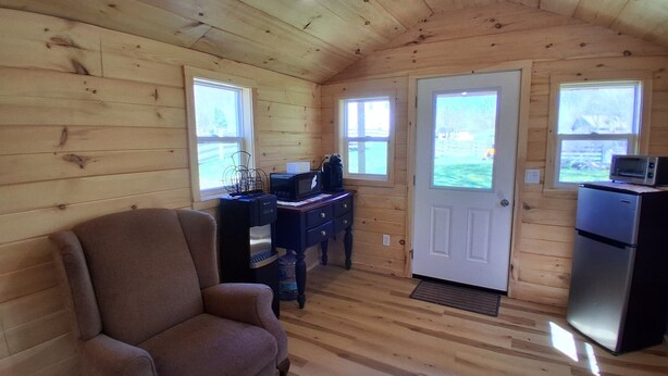 Ein gemütliches Blockhaus mit Holzwänden, einer Couch, einem Schreibtisch mit Computer, einem Kühlschrank und zwei Fenstern.