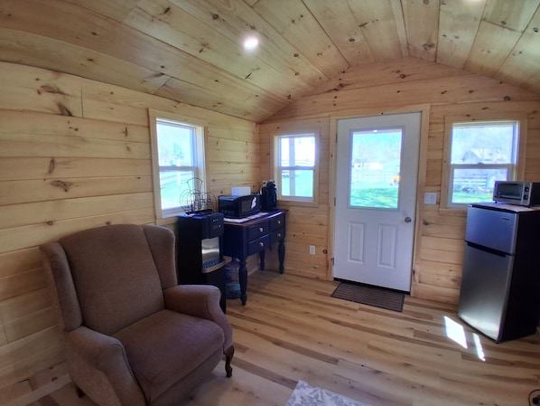 A cozy cabin with wooden walls, a sofa, a desk with a computer, a refrigerator, and two windows.