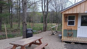Ein Holztisch für ein Picknick, ein Grill, ein kleines Holzgebäude mit einer Tür und eine Fläche mit Kies.