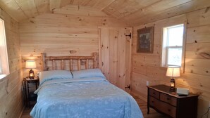 Ein Schlafzimmer einer Holzhütte mit Bett, Nachttischlampen, einem Schminktisch und einem Fenster.