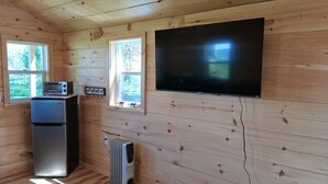 Ein Zimmer mit Holzwandverkleidung, einem Flachbildfernseher, einer kleinen Küchenzeile mit Toaster, Kühlschrank und Heizkörper.