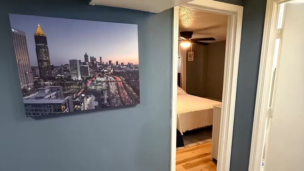 A room with a cityscape painting, wooden flooring, and a bed with a white headboard. - West Midtown Bungalow Pup Friendly (Atlanta)