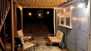 An outdoor patio with wooden furniture, a patterned rug, and string lights. - West Midtown Bungalow Pup Friendly (Atlanta)