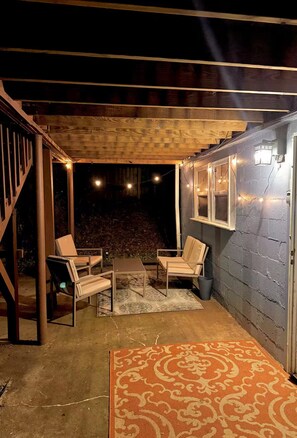Une terrasse extérieure avec des meubles en bois, un tapis à motifs et des guirlandes lumineuses.