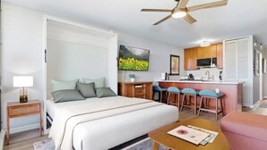 A bedroom with a bed, bedside table, and a desk with chairs. - Beautiful remodeled Kihei Condo next to the Beach! (Kihei)