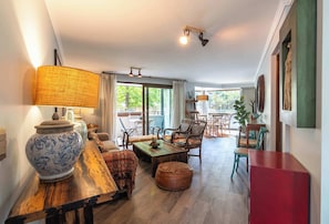 A spacious living room with a wooden coffee table, a sofa, and a large vase. There are multiple chairs and a dining table in the background.