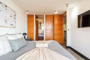 A hotel room with a bed, a TV, a wardrobe, and a bathroom visible through an open door. - HOM | Metro | Las Condes | Calefacción | Parking (Las Condes)