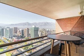 A balcony with a table and chairs, overlooking a cityscape with mountains in the background. - HOM | Pasos del Metro | Las Condes | AC | Parking (Las Condes)