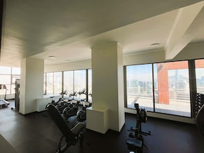 A gym with exercise equipment and large windows offering city views. - HOM | Metro | Las Condes | Calefacción | Parking (Las Condes)
