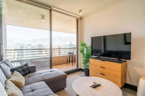 A modern living room with a sofa, a coffee table, a TV, and a potted plant. - HOM | Pasos del Metro | Las Condes | AC | Parking (Las Condes)