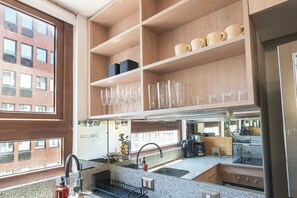 A modern kitchen with granite countertops, a stainless steel refrigerator, and a window overlooking a brick building. - HOM | LasCondes | Metro Manquehue | Parking | 1D1B (Las Condes)