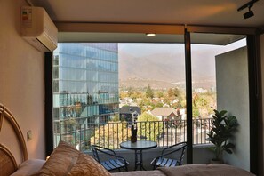 A balcony with a table and chairs, a potted plant, and a view of a modern building and mountains. - HOM I Las Condes l Parking l Wifi l Piscina l Gym (Las Condes)