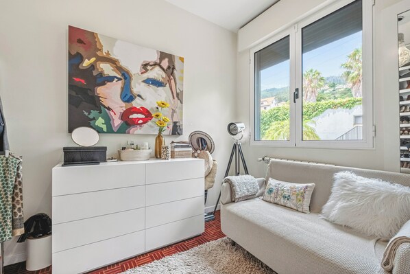 Una sala de estar moderna con un sofá blanco, un cuadro abstracto colorido, un ventanal con vistas y un armario blanco.