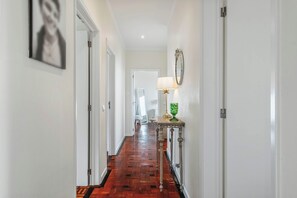 A hallway with wooden flooring, white walls, a door at the end, and a table with a lamp and vase. - Get Unforgettable Experience Private Atlantic View Pool Jacuzzi Madeira Garden (Funchal)