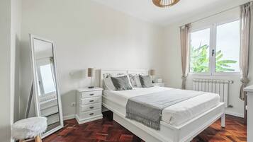 Une chambre à coucher avec un grand lit, une commode, un miroir et une fenêtre avec des rideaux.