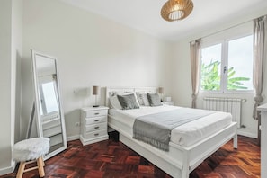 Ein Schlafzimmer mit einem großen Bett, einem Schminktisch, einem Spiegel und einem Fenster mit Vorhängen.