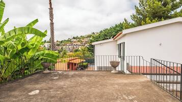 Une terrasse sur le toit avec un sol en béton, un bâtiment blanc avec une porte et une vue sur une colline parsemée de maisons.