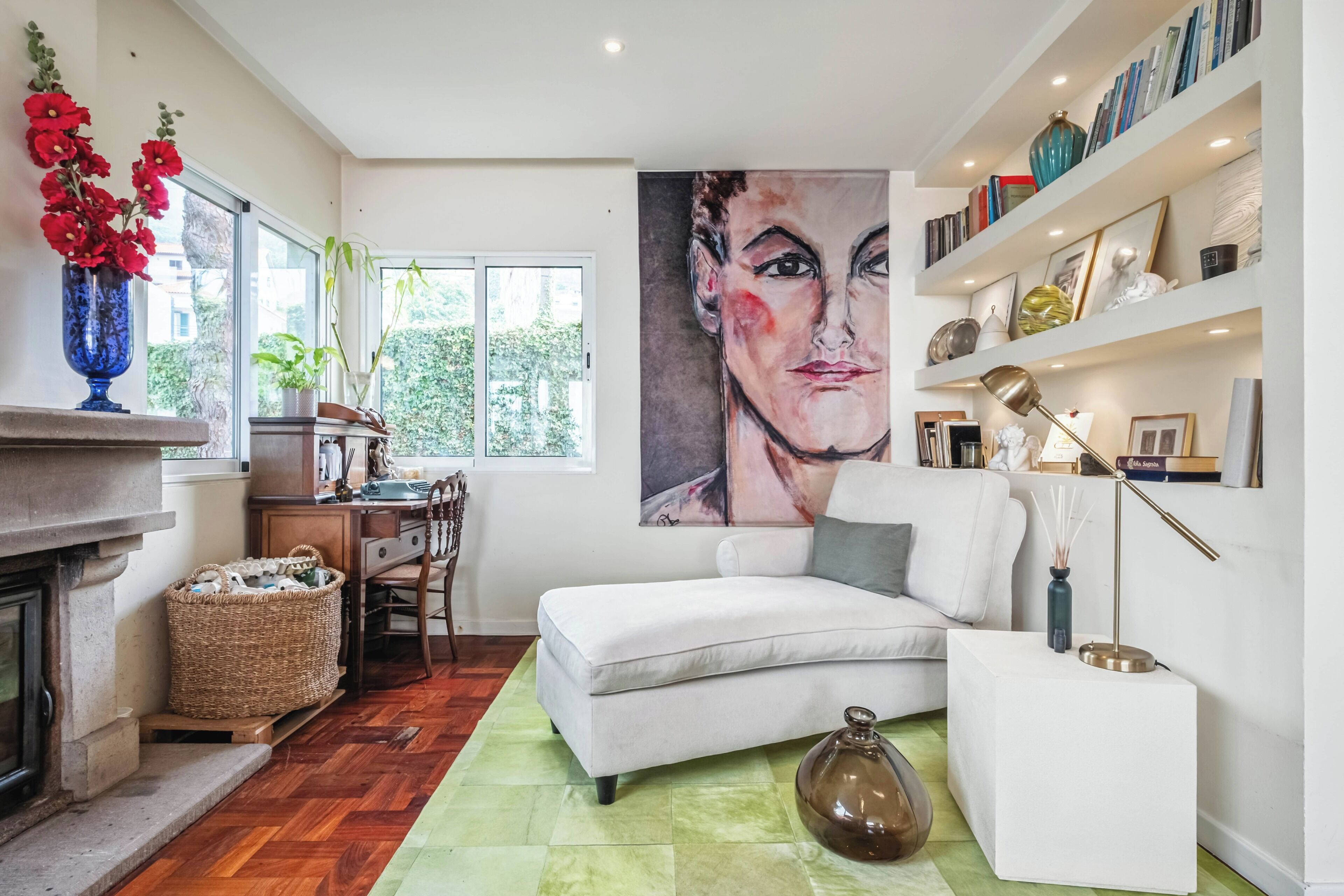 A living room with a fireplace, a sofa, a coffee table, a bookshelf, and a large painting on the wall.
