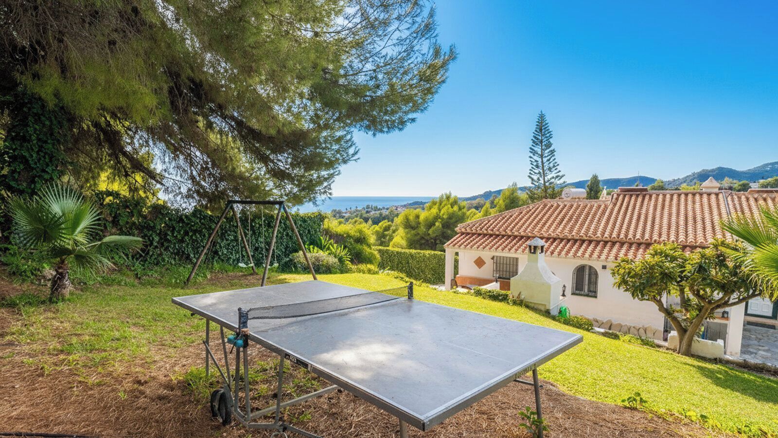 Une maison avec un toit en tuiles, un court de tennis et une vue sur la mer.