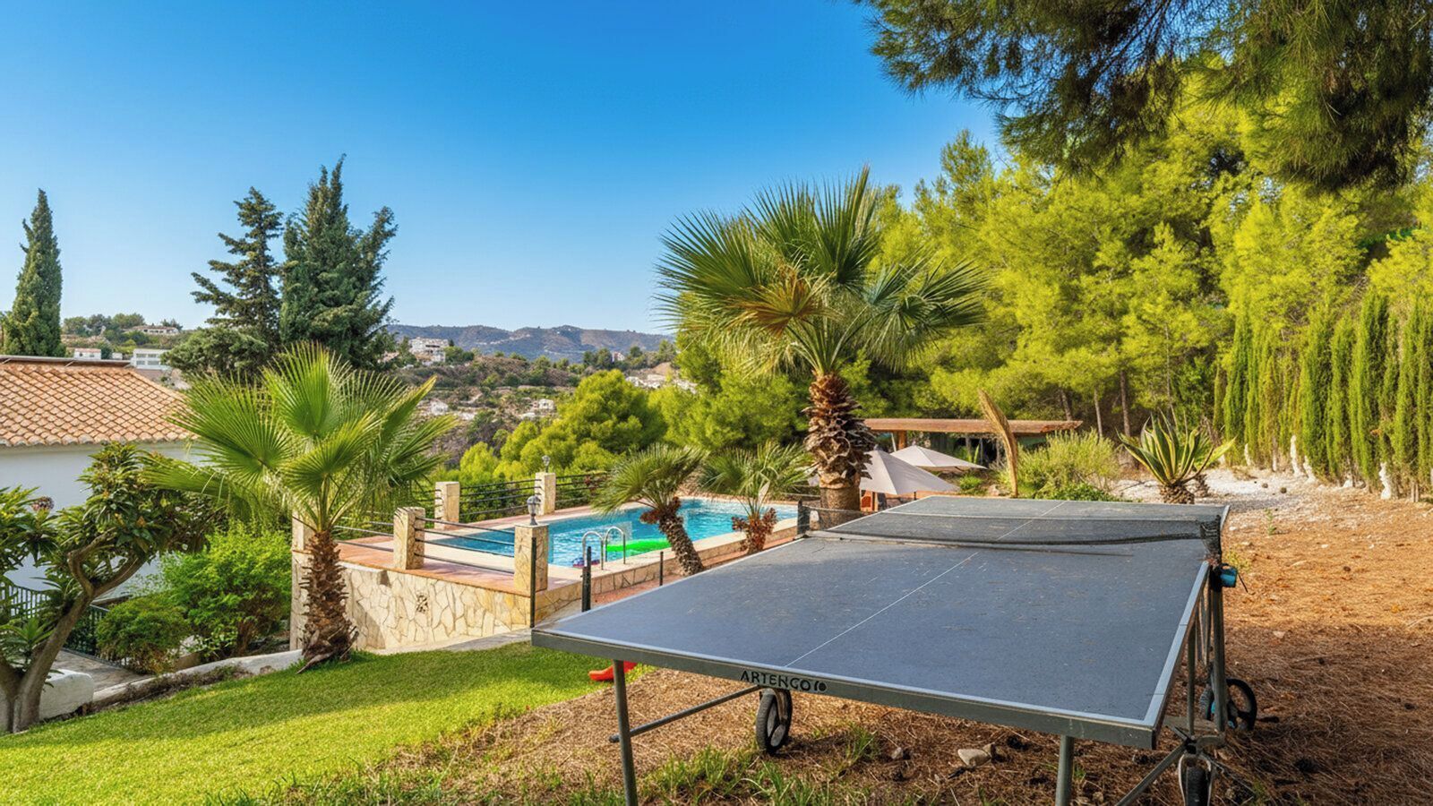 A pool with a view of a mountain range, a tennis court, and surrounding greenery.