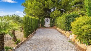 Un sendero de grava que conduce a una estructura de piedra rodeada de setos y árboles bien recortados.