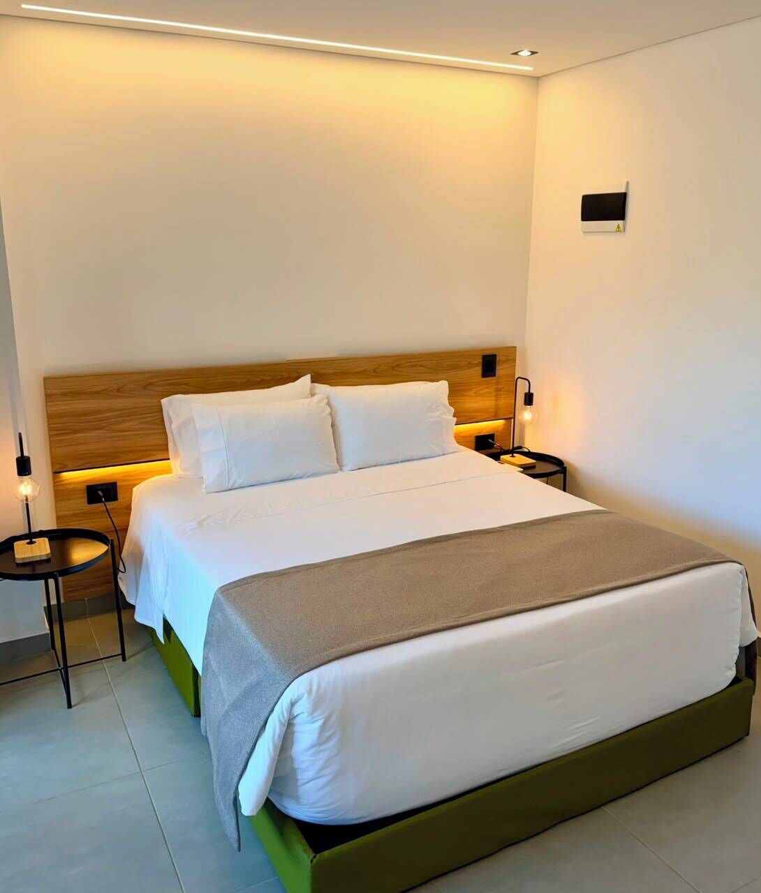 Quarto de hotel moderno com uma cama grande, mesas de cabeceira e cabeceira de madeira.