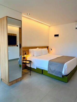 A hotel room with a bed, bedside table, lamp, and a mirror. - ONCE SUITES (Envigado)