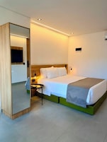 Una habitación de hotel con cama, mesita de noche, lámpara y espejo.