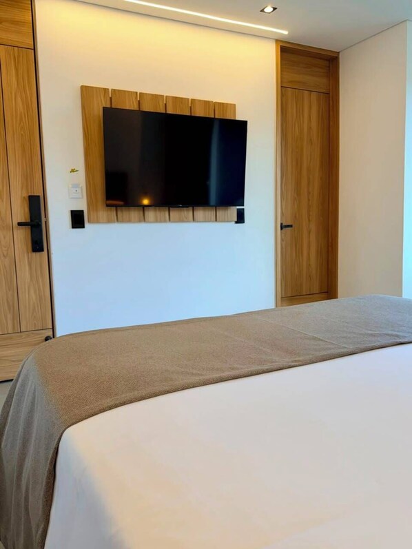 A bedroom with a bed, a television mounted on a wooden panel wall, and a wardrobe.