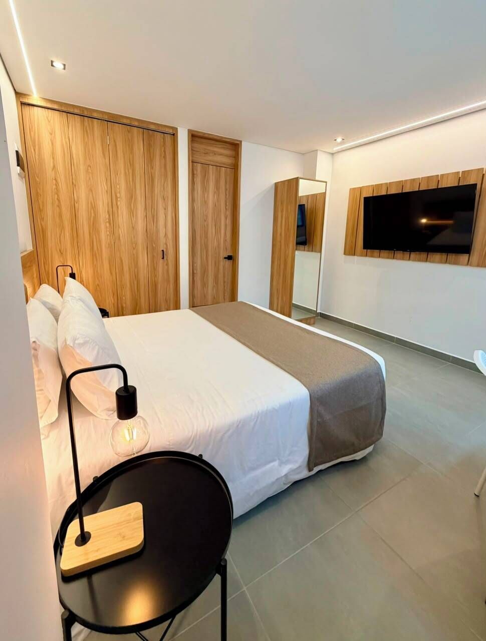 Una habitación de hotel moderna con cama, una mesita, televisor y puertas de madera.