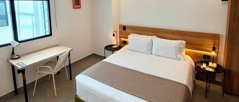 A hotel room with a bed, a desk, a chair, a nightstand, and a window.