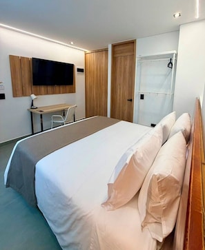 A modern hotel room with a large bed, a desk, a television mounted on the wall, and a wardrobe. - ONCE SUITES (Envigado)
