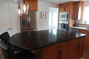 A kitchen with a central island, stainless steel appliances, wooden cabinets, and pendant lighting. - Convenient Mercer Island home loaded with amenities, 10 minutes from WC games (Mercer Island)