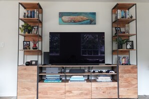 A living room with a large flat-screen TV, wooden shelving with books and decorative items, and a painting above the TV. - Convenient Mercer Island home loaded with amenities, 10 minutes from WC games (Mercer Island)