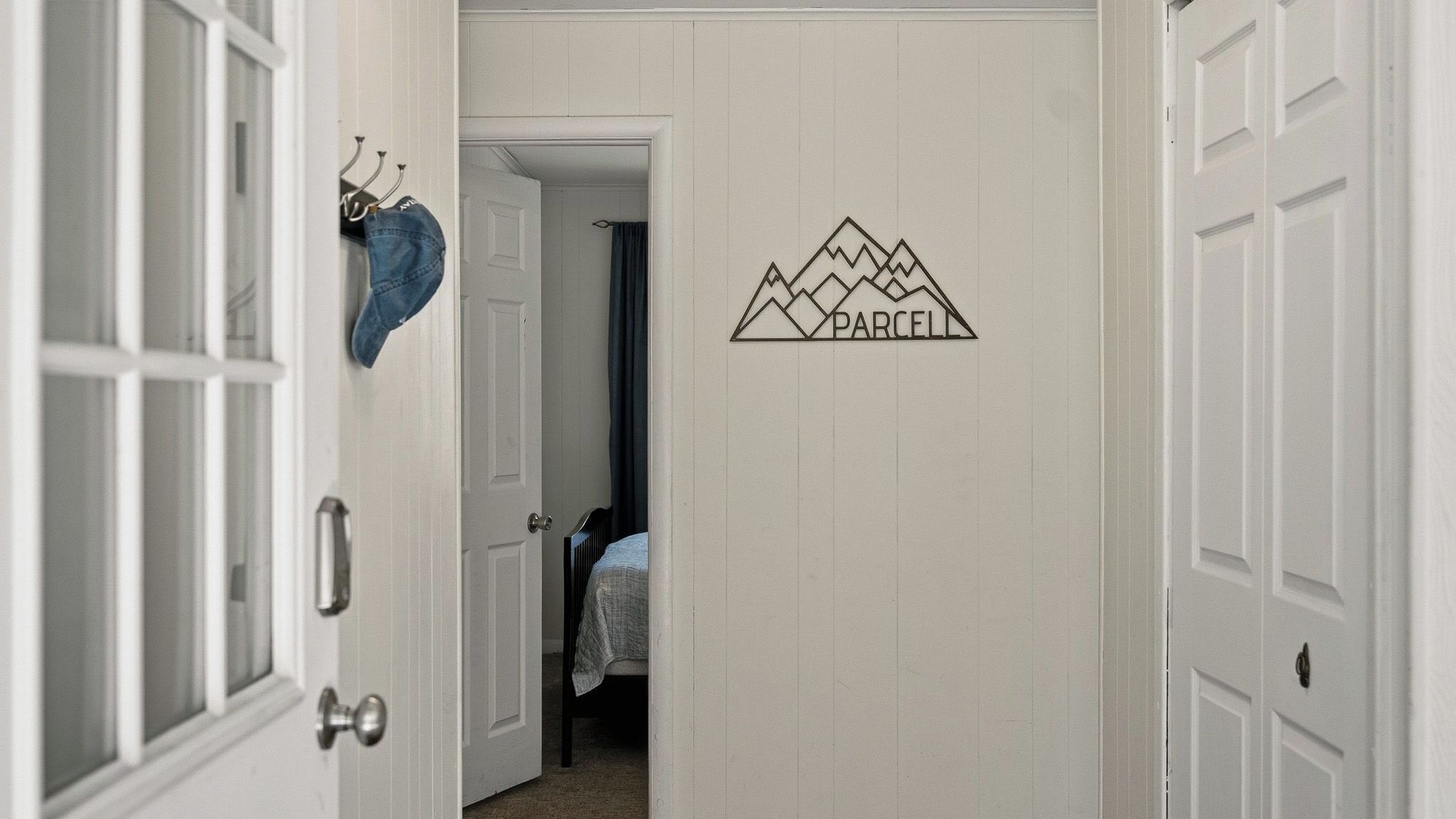 A hallway with a door leading to a bedroom, a coat rack with a jacket, and a wall decal with the word 'PARCELL'.