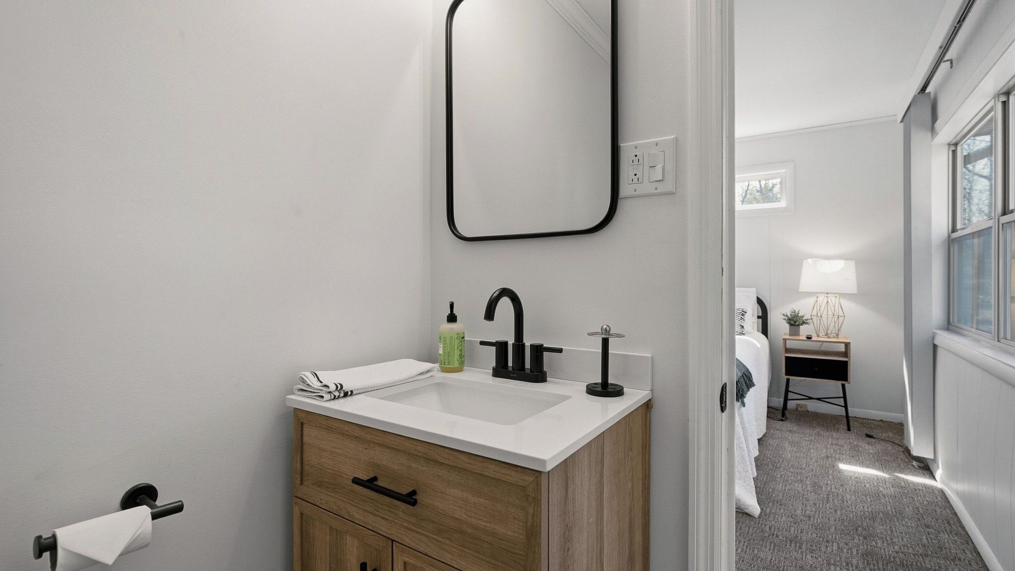 A modern bathroom with a white sink, wooden vanity, and a mirror.