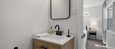 A modern bathroom with a white sink, wooden vanity, and a mirror.