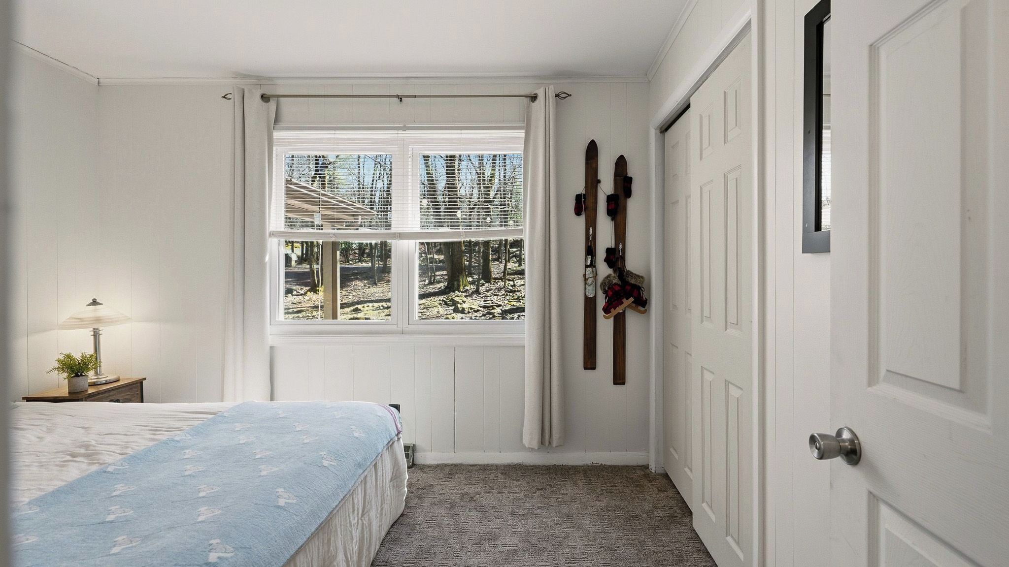 A bedroom with a bed, a window with blinds, a door, and a coat rack with items on it.