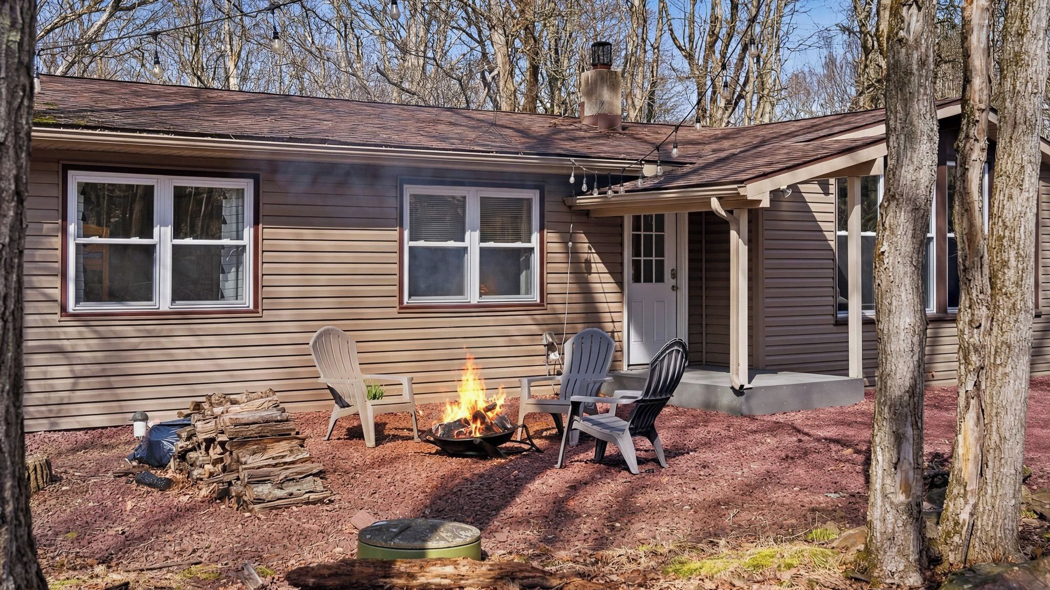 A house with a fire pit, two Adirondack chairs, and a covered porch.