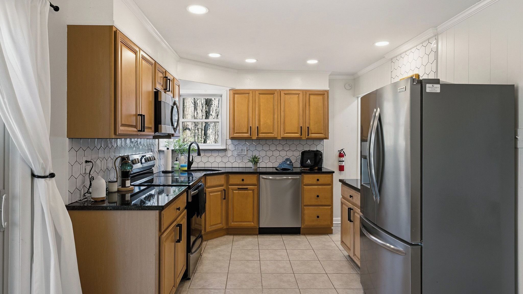 A compact kitchen with wooden cabinets, a stainless steel refrigerator, and a tiled backsplash.