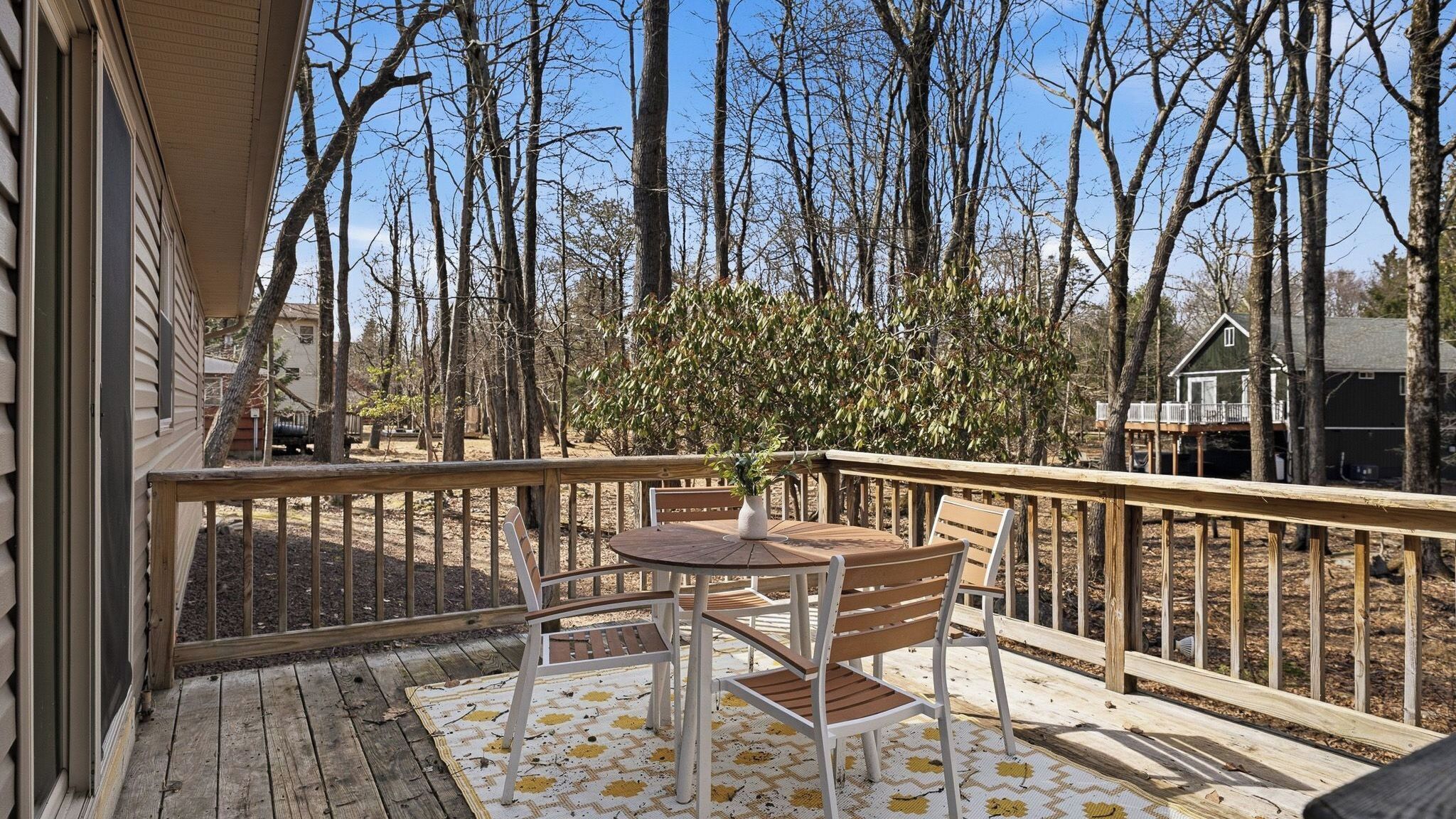A wooden deck with a table and chairs, surrounded by a wooden railing, overlooking a forested area.