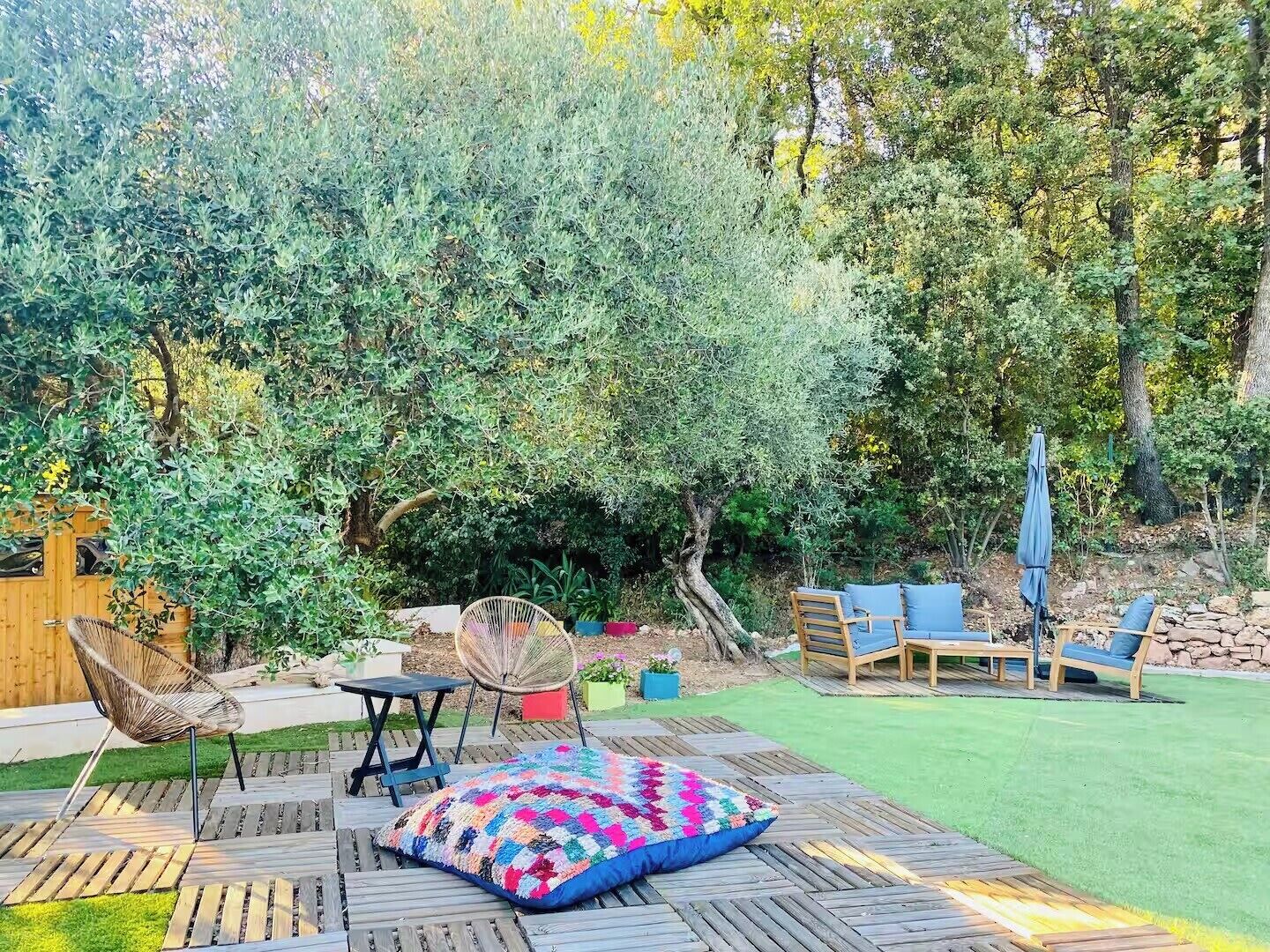 Un giardino con un patio in legno, una coperta colorata e mobili da esterno.
