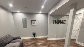 A spacious room with a herringbone wood floor, a gray sofa, and a wall-mounted sign that reads 'HOME'. - Beautiful family house with 3-bedroom  in excellent Ringgold (Ringgold)
