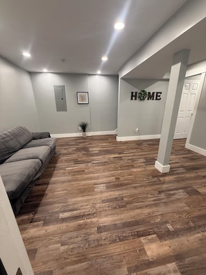A spacious room with a herringbone wood floor, a gray sofa, and a wall-mounted sign that reads 'HOME'. - Beautiful family house with 3-bedroom in excellent Ringgold (Ringgold)