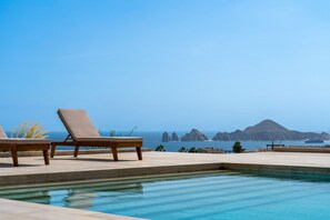 Ein Pool mit Liegestühlen und Blick auf das Meer und die Berge.