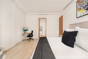 Ein modernes Schlafzimmer mit einem großen Bett, einem Schreibtisch mit Computer und Blick auf den Flur.