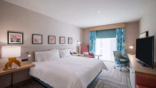 A hotel room with a bed, a desk with a computer, a chair, a TV, and framed pictures on the wall. - Hilton Garden Inn Steele Creek Charlotte (Charlotte)