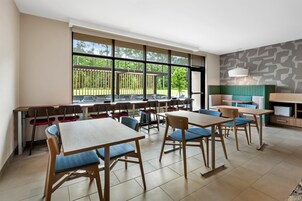 Un comedor moderno con mesas y sillas, ventanas amplias con vistas a zonas verdes y una pared con diseño.